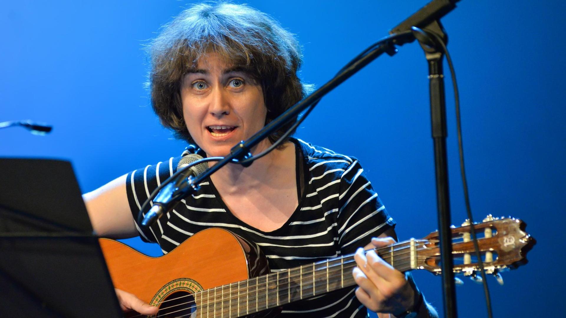 Ada Milea singt sitzend und Gitarre spielend in ein Mikrofon Ada Milea singt sitzend und Gitarre spielend in ein Mikrofon