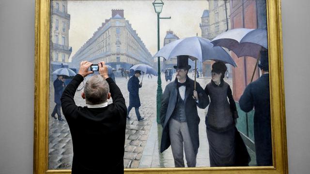 Ein Mann fotografiert das Gemälde "Straße in Paris, Regenwetter" in der Ausstellung "Gustave Caillebotte. Maler und Mäzen der Impressionisten" in der Alten Nationalgalerie in Berlin.