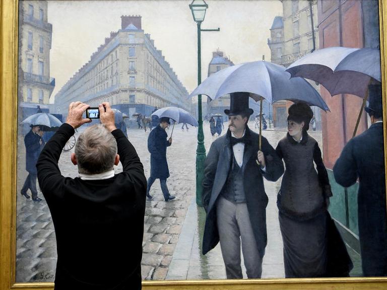 Ein Mann fotografiert das Gemälde "Straße in Paris, Regenwetter" in der Ausstellung "Gustave Caillebotte. Maler und Mäzen der Impressionisten" in der Alten Nationalgalerie in Berlin.
