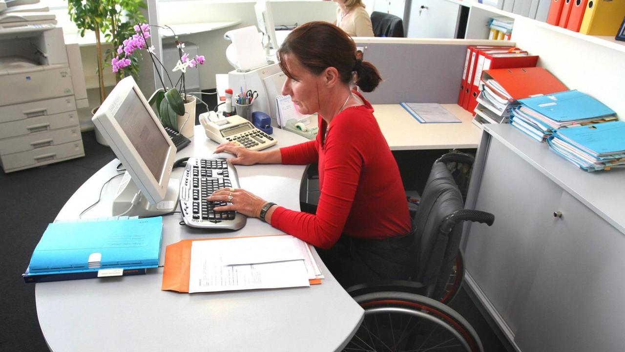 Eine Frau im Rollstuhl arbeitet am Computer im Büro Eine Frau im Rollstuhl arbeitet am Computer im Büro
