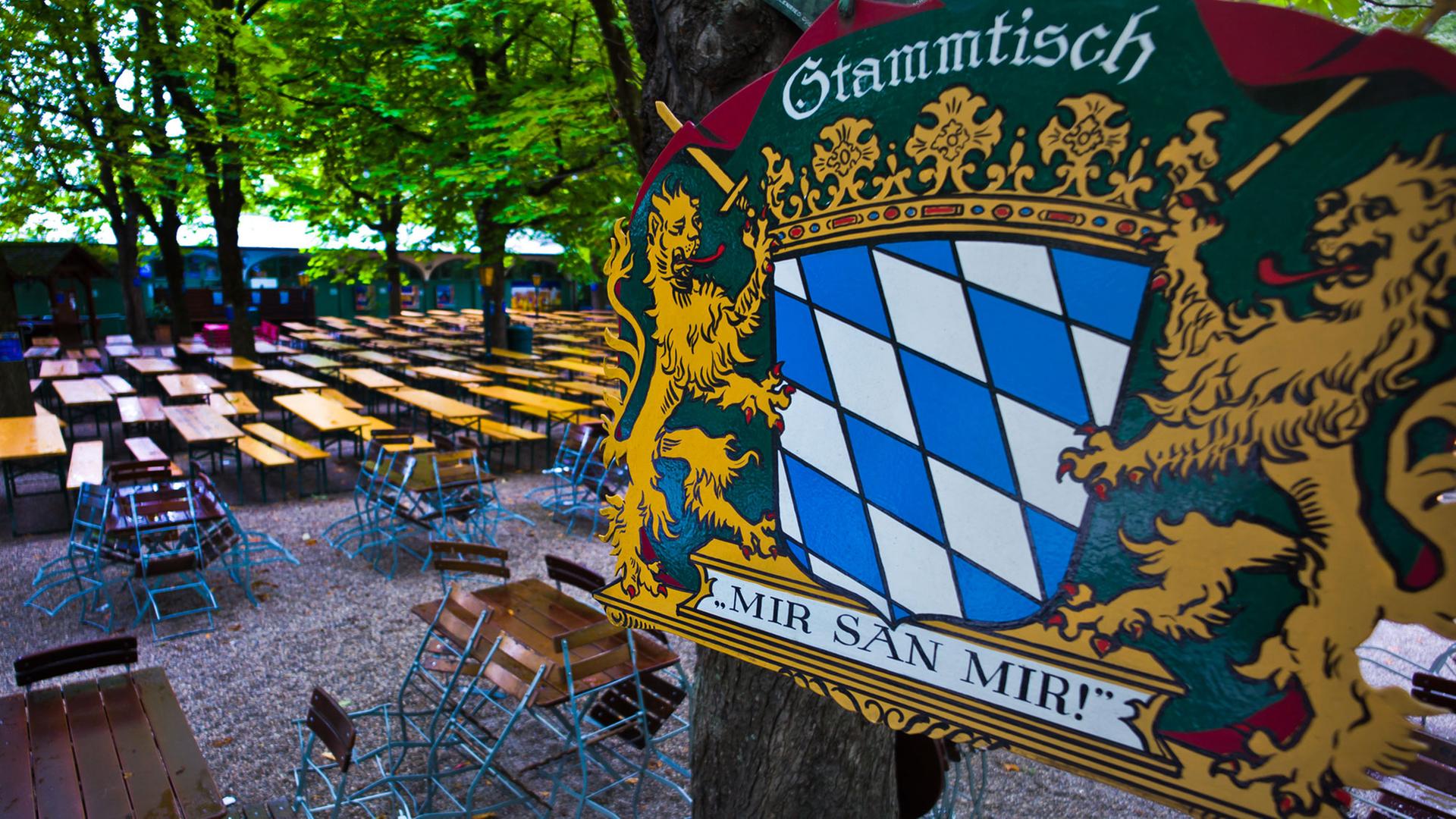 Ein Metallschild mit der Aufschrift "Stammtisch - Mir san mir!" hängt bei Regen in München über einem leeren Biergarten. Ein Metallschild mit der Aufschrift "Stammtisch - Mir san mir!" hängt bei Regen in München über einem leeren Biergarten.