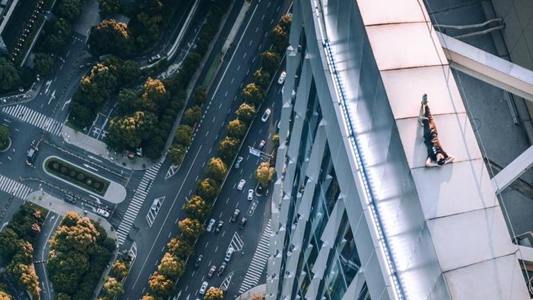 Ein junger Mensch liegt entspannt am Rand eines Hochhaus-Daches und genieß die Sonne, während gleich neben ihm eine perspektivisch beeindruckende Tiefe gähnt. Ein junger Mensch liegt entspannt am Rand eines Hochhaus-Daches und genieß die Sonne, während gleich neben ihm eine perspektivisch beeindruckende Tiefe gähnt.