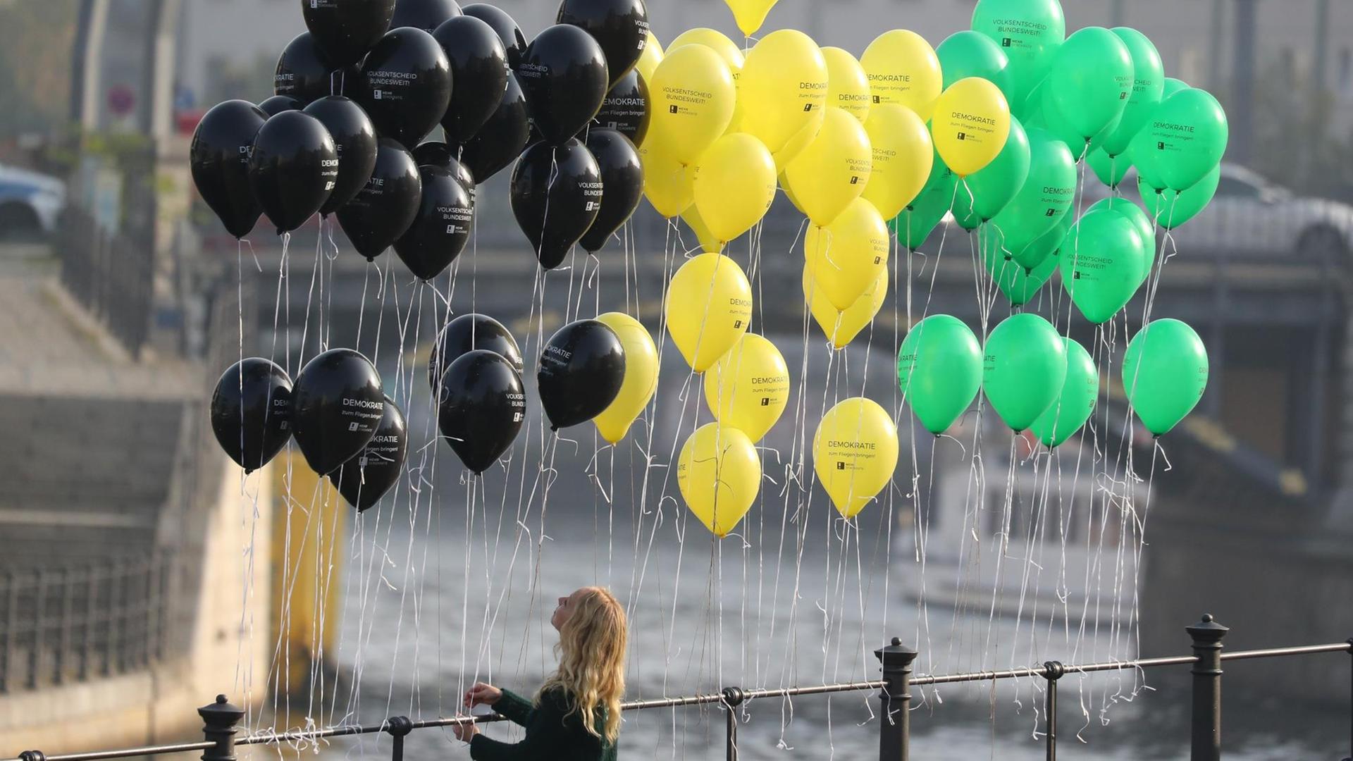 Eine junge Frau befestigt in Berlin Luftballons in den Jamaika-Farben an einem Geländer bei der Parlamentarischen Gesellschaft an der Spree. Eine junge Frau befestigt in Berlin Luftballons in den Jamaika-Farben an einem Geländer bei der Parlamentarischen Gesellschaft an der Spree.