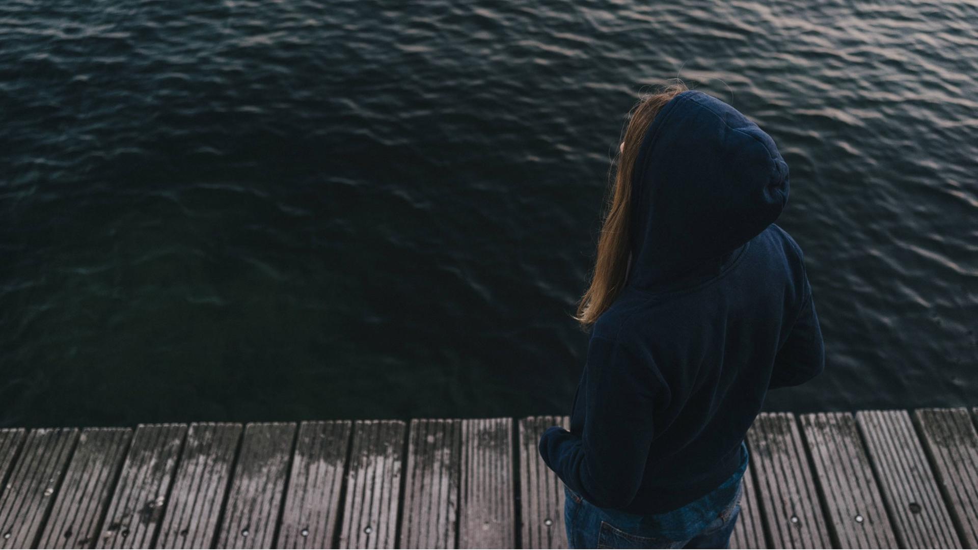 Eine junge Frau auf einem Steg blickt ins Wasser Eine junge Frau auf einem Steg blickt ins Wasser