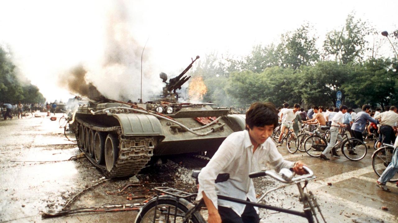 Menschen mit Fahrrädern neben einem in Brand gesetzten Panzer westlich des Tien An Men-Platzes in Peking (Foto vom 4.6.1989). Chinesisches Militär hatte am 4.6.1989 auf dem Platz des Himmlischen Friedens (Tien An Men) in Peking, auf dem Studenten für mehr Demokratie, Pressefreiheit und gegen Parteiprivilegien demonstrierten, ein Blutbad angerichtet. Menschen mit Fahrrädern neben einem in Brand gesetzten Panzer westlich des Tien An Men-Platzes in Peking (Foto vom 4.6.1989). Chinesisches Militär hatte am 4.6.1989 auf dem Platz des Himmlischen Friedens (Tien An Men) in Peking, auf dem Studenten für mehr Demokratie, Pressefreiheit und gegen Parteiprivilegien demonstrierten, ein Blutbad angerichtet.