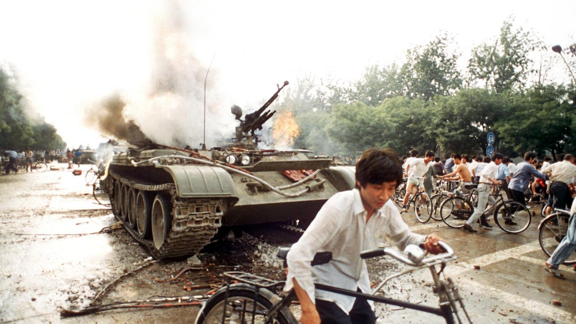 Menschen mit Fahrrädern neben einem in Brand gesetzten Panzer westlich des Tien An Men-Platzes in Peking (Foto vom 4.6.1989). Chinesisches Militär hatte am 4.6.1989 auf dem Platz des Himmlischen Friedens (Tien An Men) in Peking, auf dem Studenten für mehr Demokratie, Pressefreiheit und gegen Parteiprivilegien demonstrierten, ein Blutbad angerichtet. Menschen mit Fahrrädern neben einem in Brand gesetzten Panzer westlich des Tien An Men-Platzes in Peking (Foto vom 4.6.1989). Chinesisches Militär hatte am 4.6.1989 auf dem Platz des Himmlischen Friedens (Tien An Men) in Peking, auf dem Studenten für mehr Demokratie, Pressefreiheit und gegen Parteiprivilegien demonstrierten, ein Blutbad angerichtet.