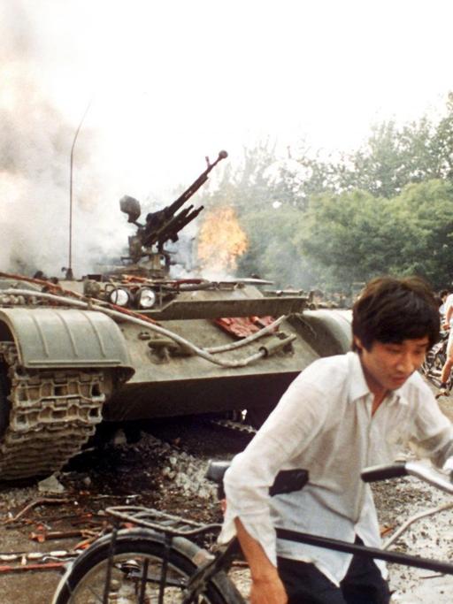 Menschen mit Fahrrädern neben einem in Brand gesetzten Panzer westlich des Tien An Men-Platzes in Peking (Foto vom 4.6.1989). Chinesisches Militär hatte am 4.6.1989 auf dem Platz des Himmlischen Friedens (Tien An Men) in Peking, auf dem Studenten für mehr Demokratie, Pressefreiheit und gegen Parteiprivilegien demonstrierten, ein Blutbad angerichtet.