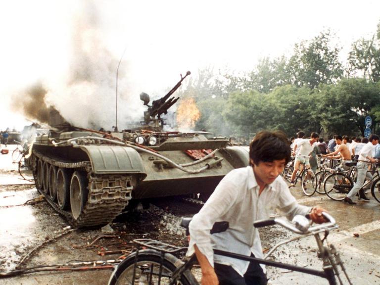 Menschen mit Fahrrädern neben einem in Brand gesetzten Panzer westlich des Tien An Men-Platzes in Peking (Foto vom 4.6.1989). Chinesisches Militär hatte am 4.6.1989 auf dem Platz des Himmlischen Friedens (Tien An Men) in Peking, auf dem Studenten für mehr Demokratie, Pressefreiheit und gegen Parteiprivilegien demonstrierten, ein Blutbad angerichtet.
