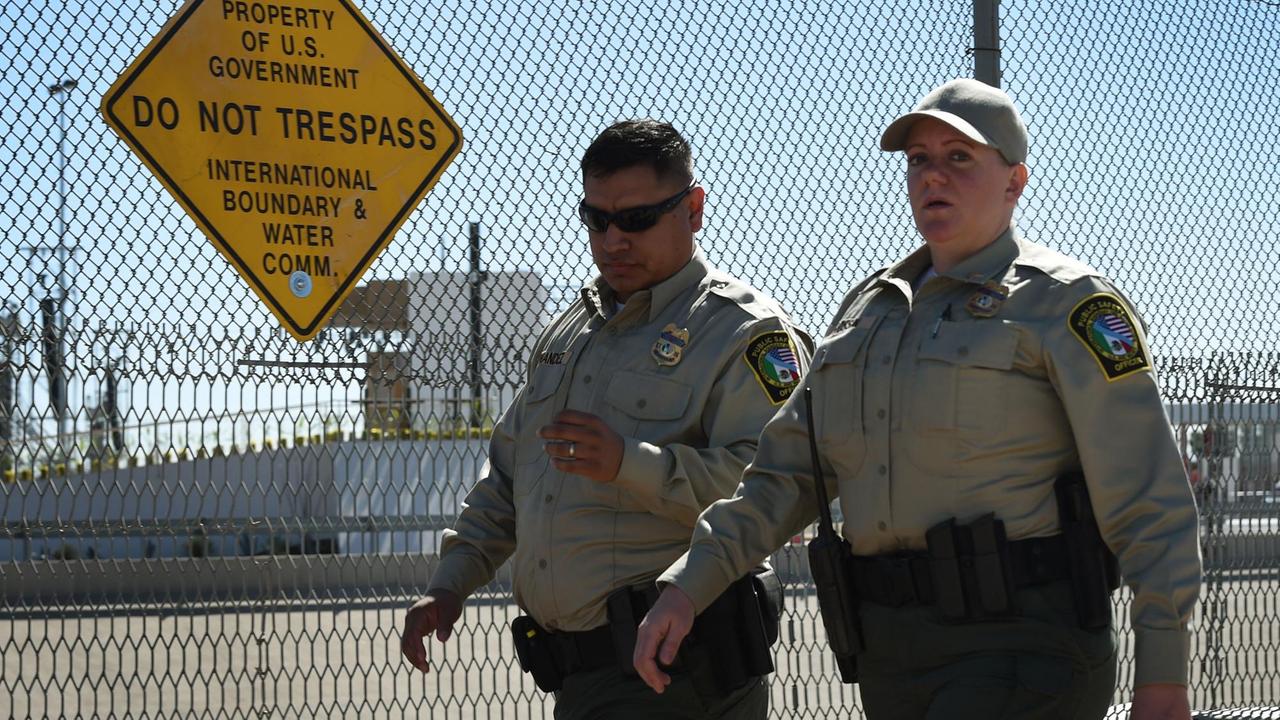 Sicherheitskräfte in Uniform gehen an einem Stacheldrahtzaun entlang. Daran hängt ein gelbes Schild mit schwarzer Aufschrift, wonach der Grenzübertritt verboten ist.