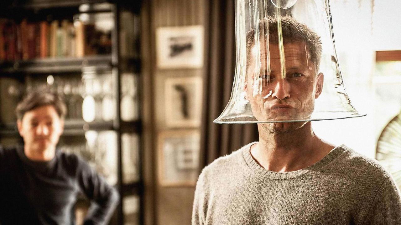 Til Schweiger trägt eine Glocke aus Glas auf dem Kopf und grinst in die Kamera. Til Schweiger trägt eine Glocke aus Glas auf dem Kopf und grinst in die Kamera.