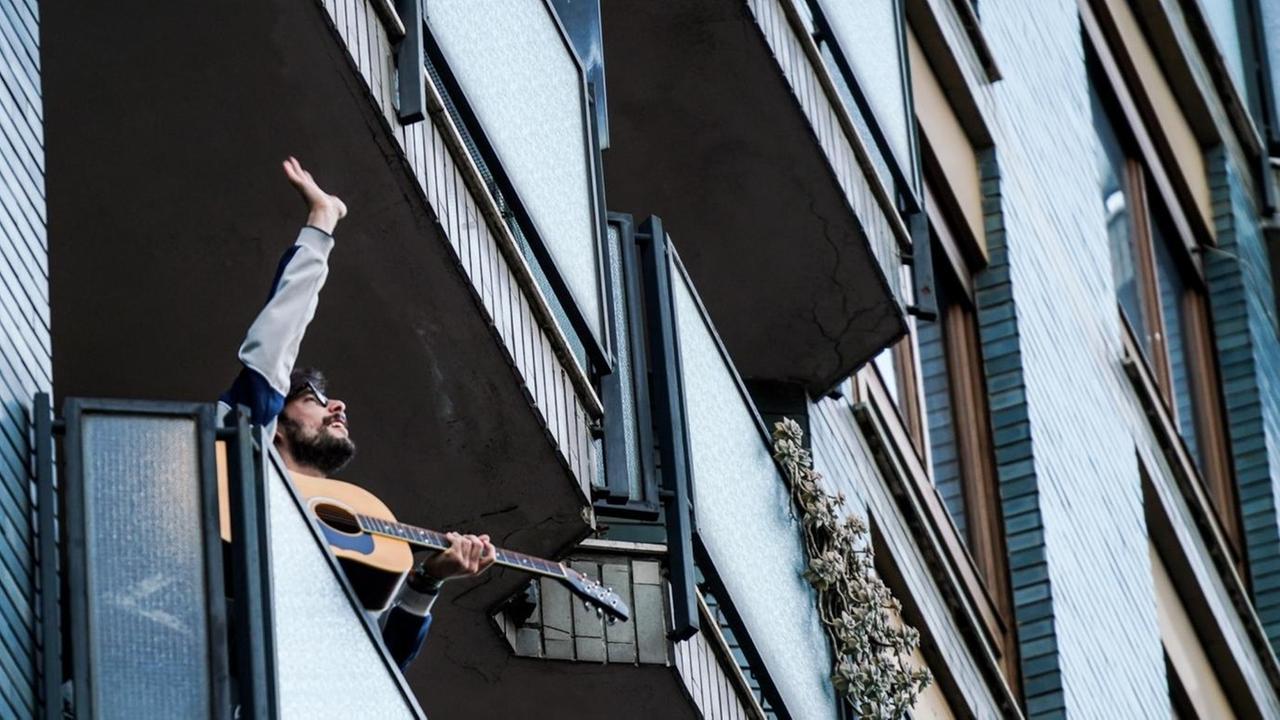 Ein Gitarrist steht auf einem Balkon in Mailand, Italien, und spielt für seine Nachbarschaft. Ein Gitarrist steht auf einem Balkon in Mailand, Italien, und spielt für seine Nachbarschaft.