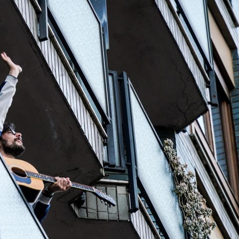 Ein Gitarrist steht auf einem Balkon in Mailand, Italien, und spielt für seine Nachbarschaft.