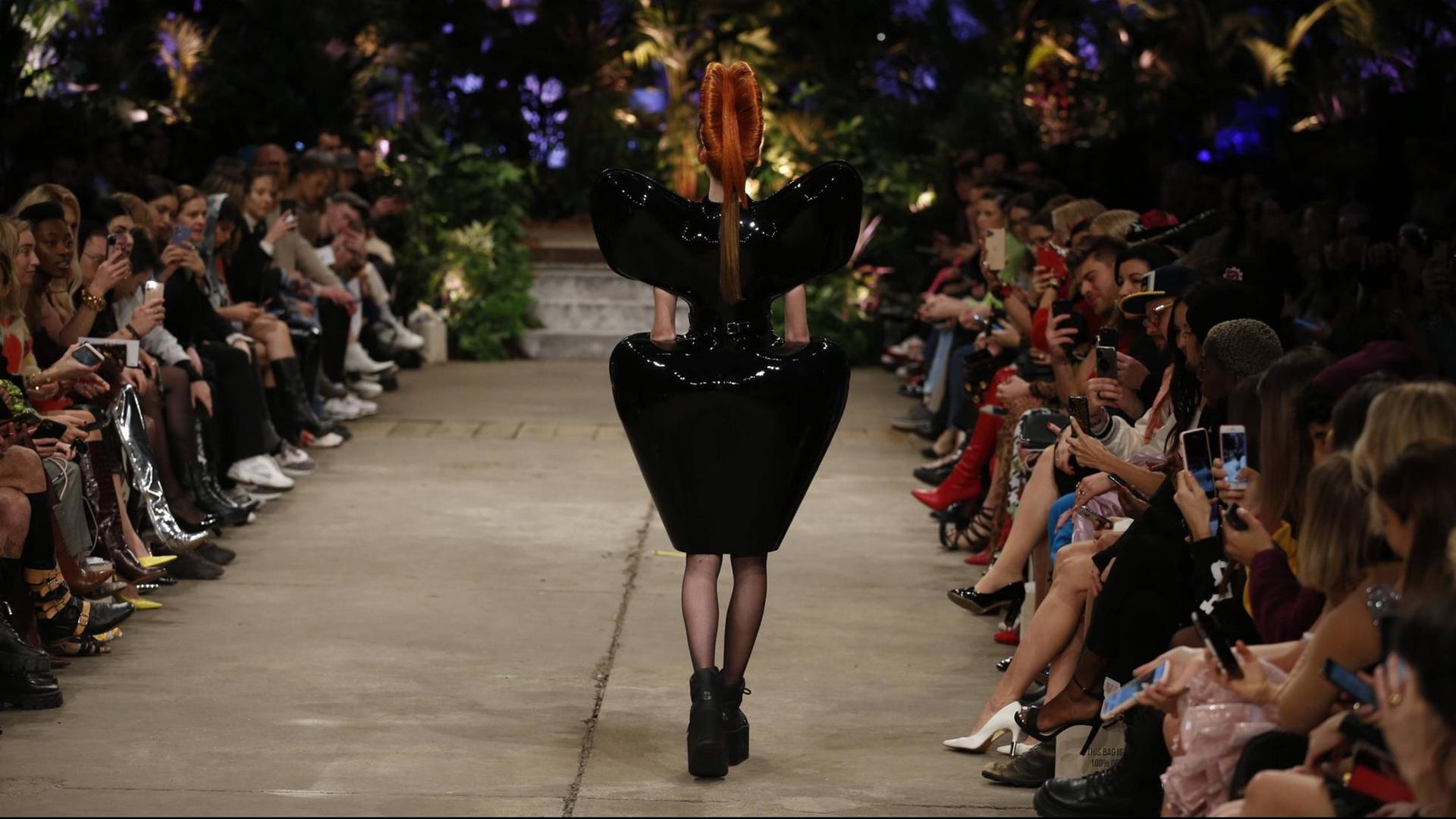 Eine Frau in einem extravaganten schwarzen Kleid in einer Rückenansicht auf dem Laufsteg. Eine Frau in einem extravaganten schwarzen Kleid in einer Rückenansicht auf dem Laufsteg.