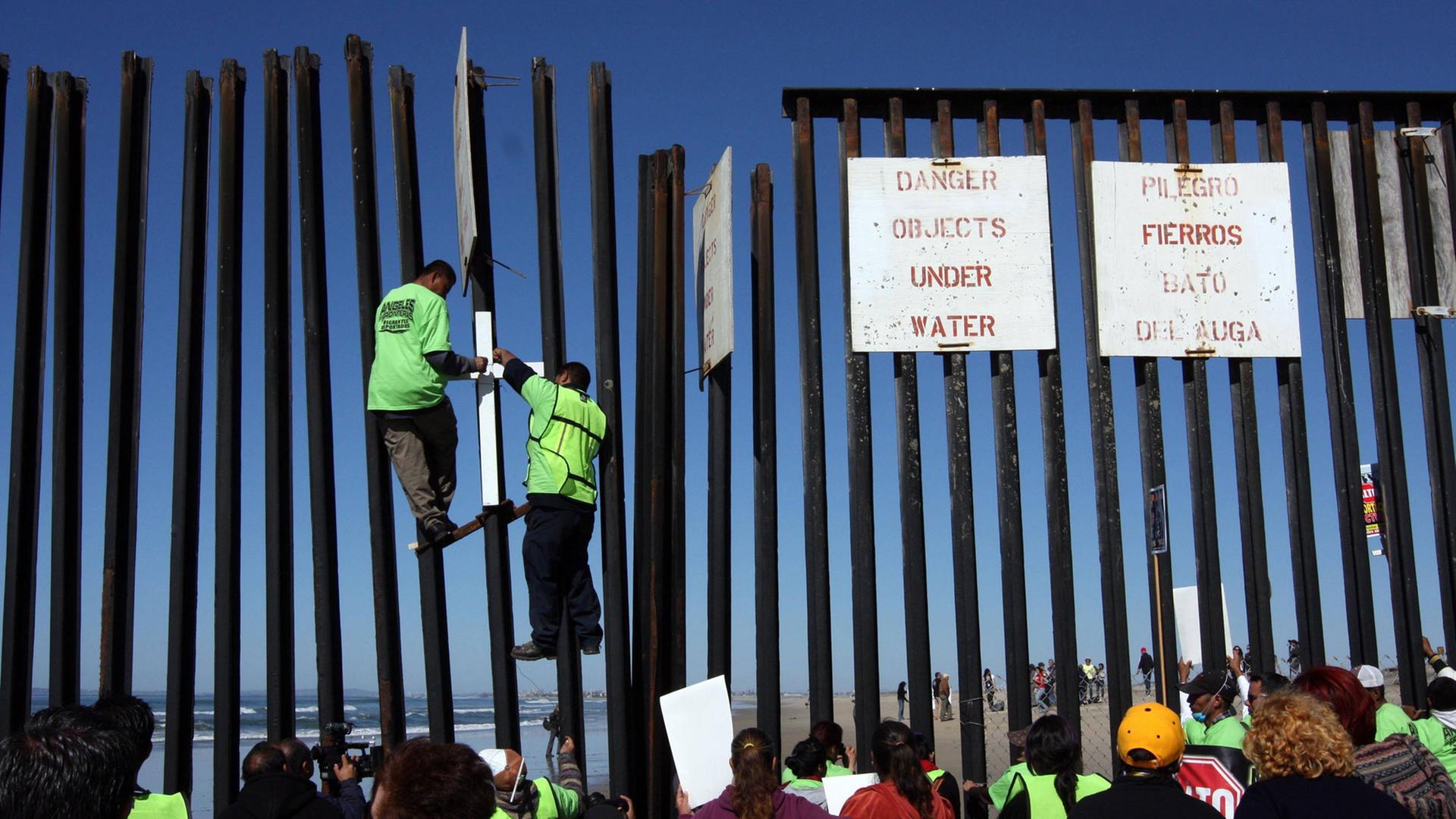 Zwei Migranten klettern am amerikanisch-mexikanischen Grenzzaun auf der mexikanischen Seite hoch. Zwei Migranten klettern am amerikanisch-mexikanischen Grenzzaun auf der mexikanischen Seite hoch.