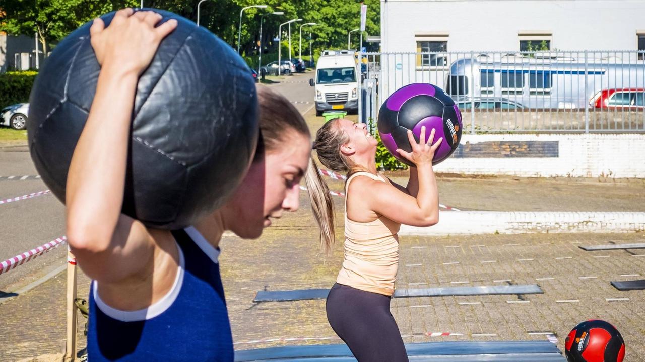 Zwei junge Frauen trainieren mit Medizinbällen, die Frau im Hintergrund sichtlich angestrengt. Zwei junge Frauen trainieren mit Medizinbällen, die Frau im Hintergrund sichtlich angestrengt.
