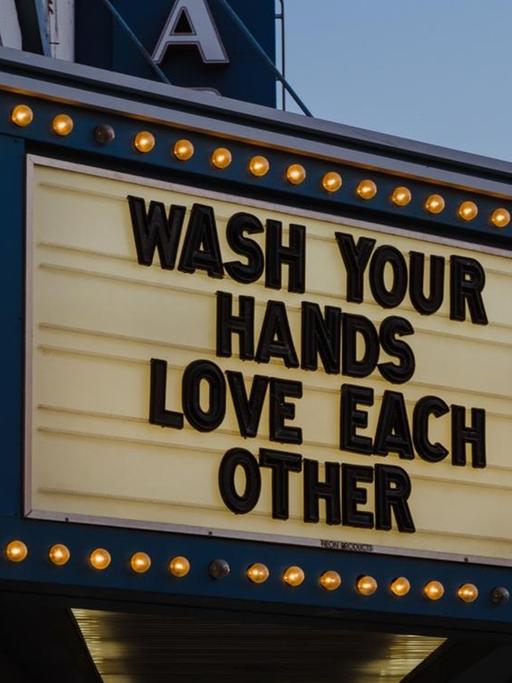 "Wash your hands. Love each other" steht als Schriftzug an einem Theatereingang.