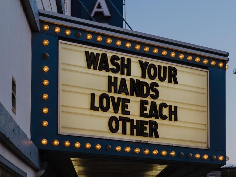 "Wash your hands. Love each other" steht als Schriftzug an einem Theatereingang.