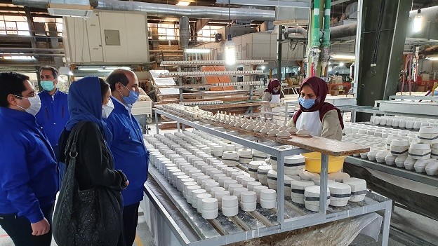 Mehrere Leute in azurblauen Kitteln stehen vor einem Tisch mit Porzellanprodukten in Arbeit.