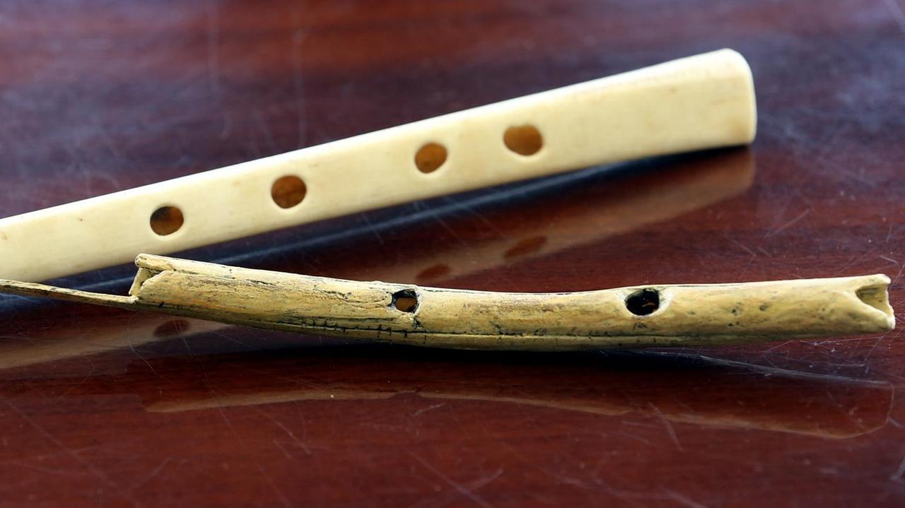 Der Nachbau einer 38000 Jahre alten Flöte aus Geierflügelknochen (oben) und eine Flöte aus Mammutelfenbein liegen nebeneinander auf einem dunklen Holztisch. Der Nachbau einer 38000 Jahre alten Flöte aus Geierflügelknochen (oben) und eine Flöte aus Mammutelfenbein liegen nebeneinander auf einem dunklen Holztisch.
