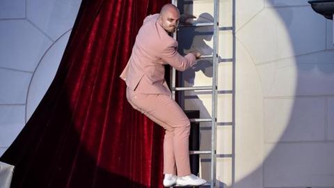 Tartuffe klettert eine Leiter herunter, die an die Fassade des Deutschen Theaters gelehnt ist.