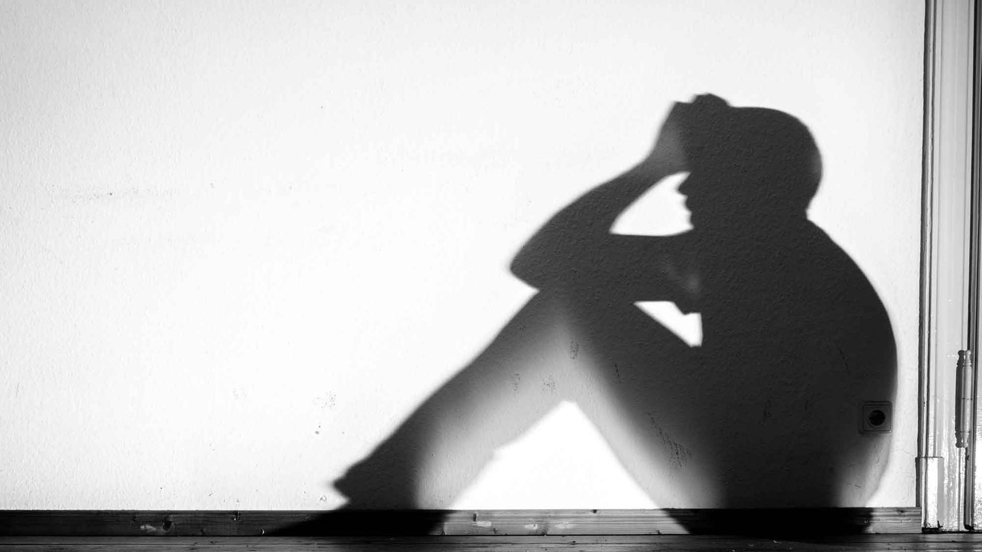 Ein Mensch sitzt auf einer Fensterbank und stützt seinen Kopf mit den Armen, im Gegenlicht sind nur seine Umrisse erkennbar. Ein Mensch sitzt auf einer Fensterbank und stützt seinen Kopf mit den Armen, im Gegenlicht sind nur seine Umrisse erkennbar.