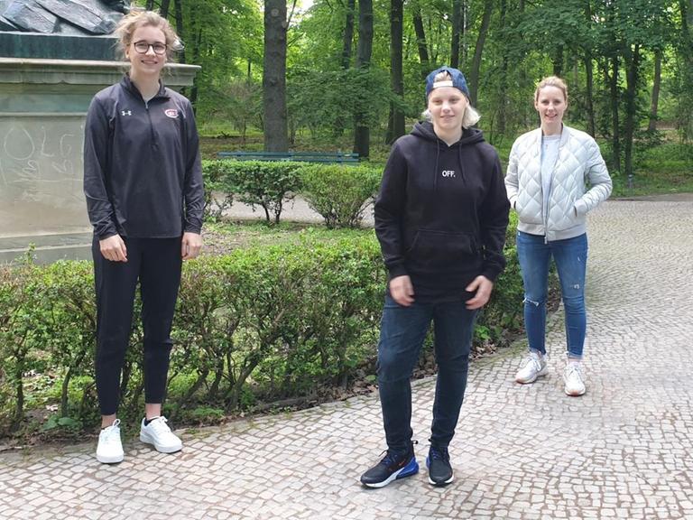 Drei Frauen stehen in ziviler Kleidung im Park und lächeln in die Kamera