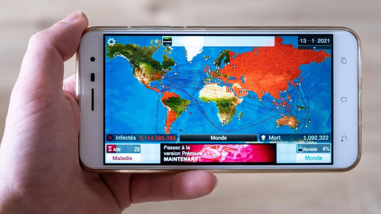 Auf einem Handy-Bildschirm ist in einem Spiel eine Weltkarte zu sehen, auf der Übertragungswege einer Seuche zu sehen sind. Auf einem Handy-Bildschirm ist in einem Spiel eine Weltkarte zu sehen, auf der Übertragungswege einer Seuche zu sehen sind.