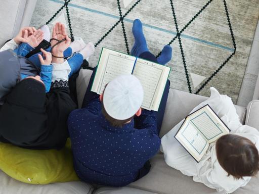 Blick von oben auf eine junge muslimische Familie, die während des Ramadan im Koran lesen. (Symbolbild)