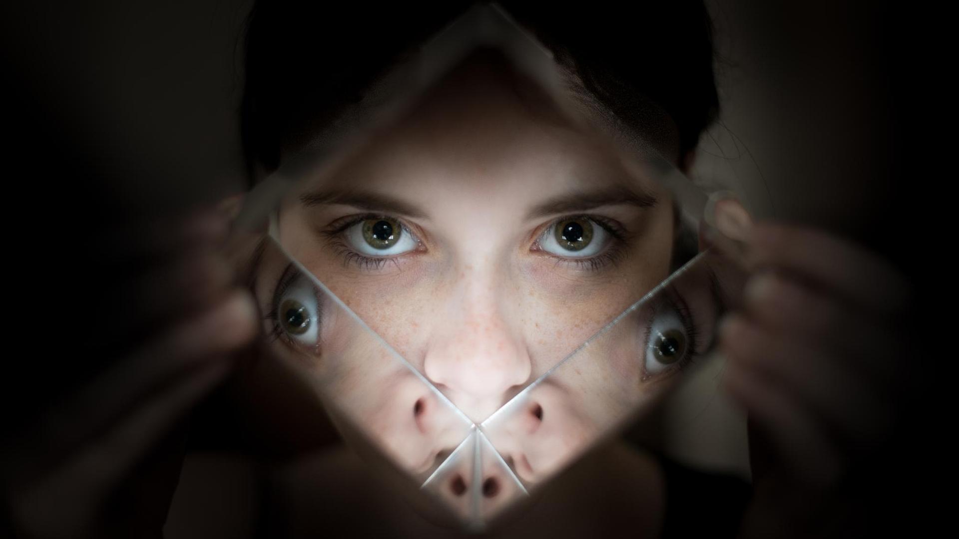 Eine Frau schaut durch ein Prisma, in dem sich ihre Augen spiegeln.