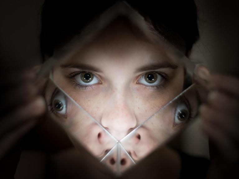 Eine Frau schaut durch ein Prisma, in dem sich ihre Augen spiegeln.