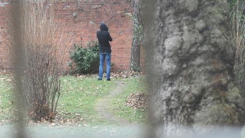 Ein Mann steht mit dem Rücken zur Kamera an einer Wand in einem Garten.