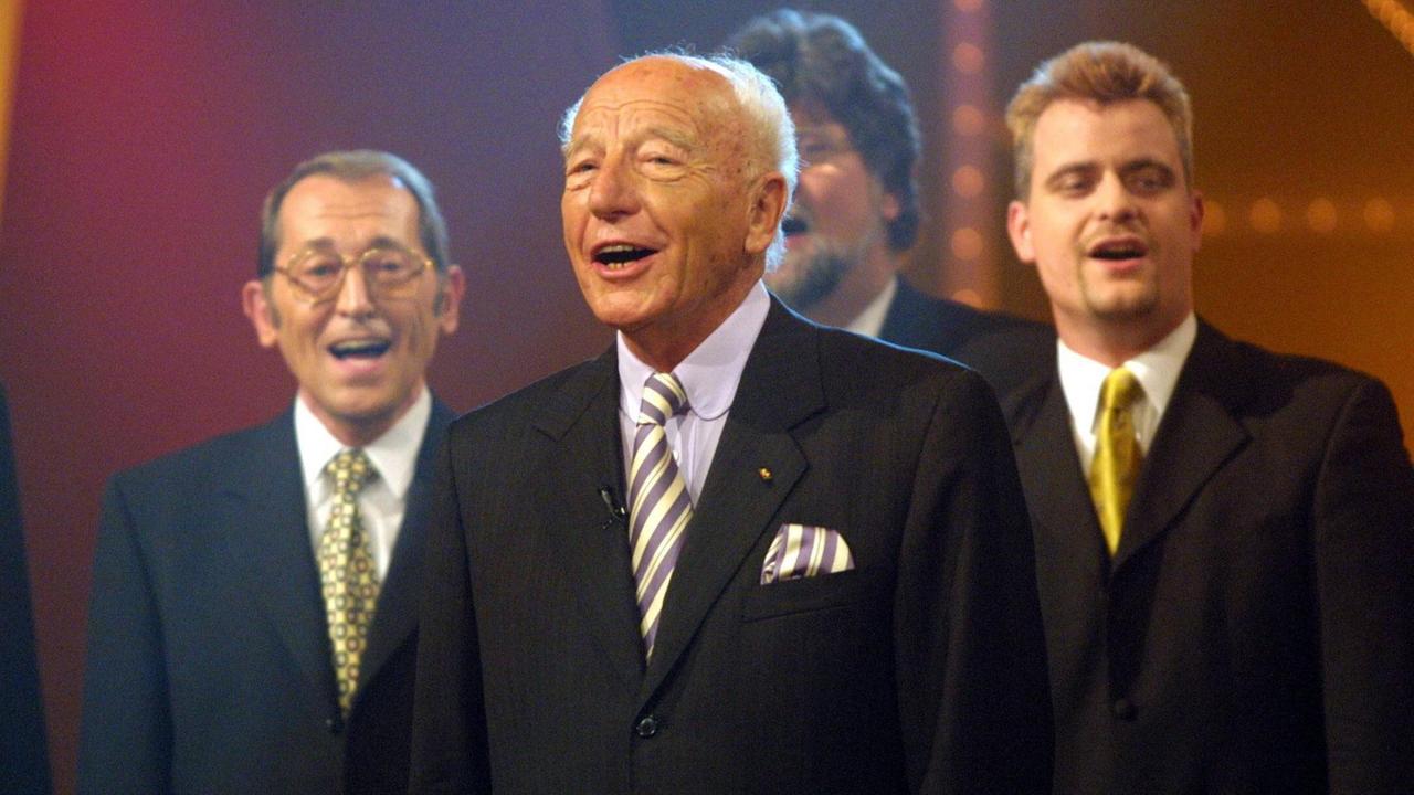 Ein älterer Mann singt, im Hindergrund singen mit ihm ein älterer Mann und ein jüngerer Mann
