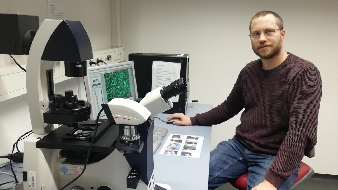 Tobias Fromme sitzt im "Quantum Brain"-Labor der TU München vor einem Arbeitstisch, auf dem links das Mikroskop steht
