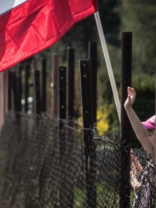 Blick auf den Zaun am ehemaligen Konzentrationslager Auschwitz - ein Kind winkt mit einer polnischen Fahne.