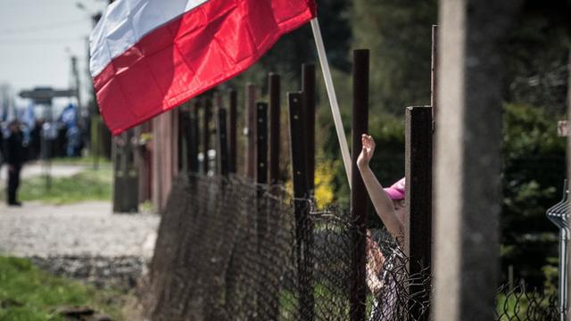 Blick auf den Zaun am ehemaligen Konzentrationslager Auschwitz - ein Kind winkt mit einer polnischen Fahne.