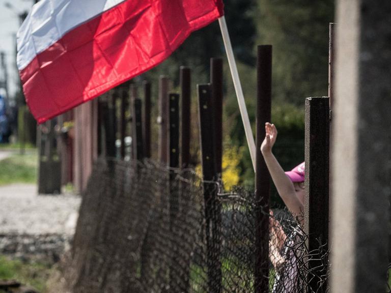 Blick auf den Zaun am ehemaligen Konzentrationslager Auschwitz - ein Kind winkt mit einer polnischen Fahne.