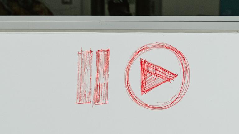 Das Logo für "Play Pause /Abspielen anhalten" ist mit rotem Stift auf einen hellgrauen Hintergrung gezeichnet. Das Logo für "Play Pause /Abspielen anhalten" ist mit rotem Stift auf einen hellgrauen Hintergrung gezeichnet.