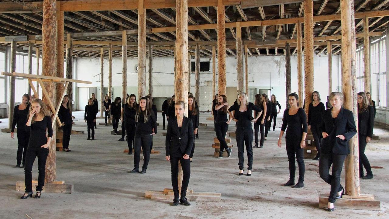 Die Sängerinnen des Chores stehen in einer Halle deren Decke von Holzstützen abgestützt wird. Die Sängerinnen des Chores stehen in einer Halle deren Decke von Holzstützen abgestützt wird.