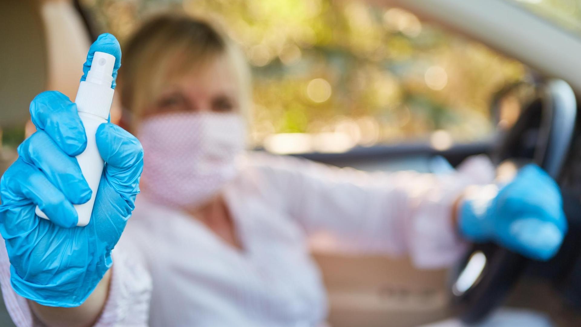 Frau im Auto mit Mundschutz und Desinfektionsmittel Frau im Auto mit Mundschutz und Desinfektionsmittel