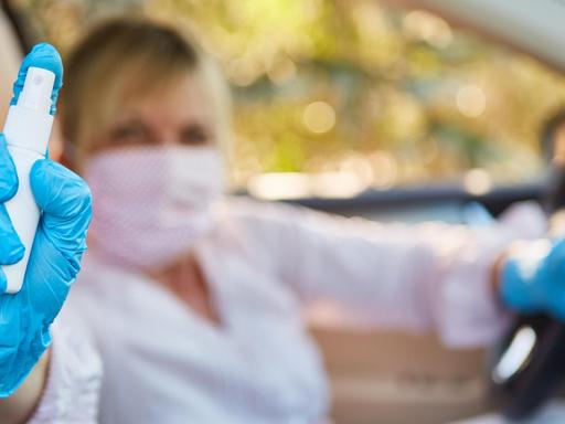 Frau im Auto mit Mundschutz und Desinfektionsmittel