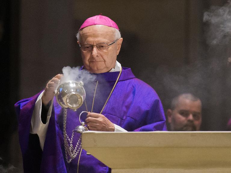 Robert Zollitsch schwenkt in violettem Ornat mit roter Kappe ein Weihrauchfass am Altar
