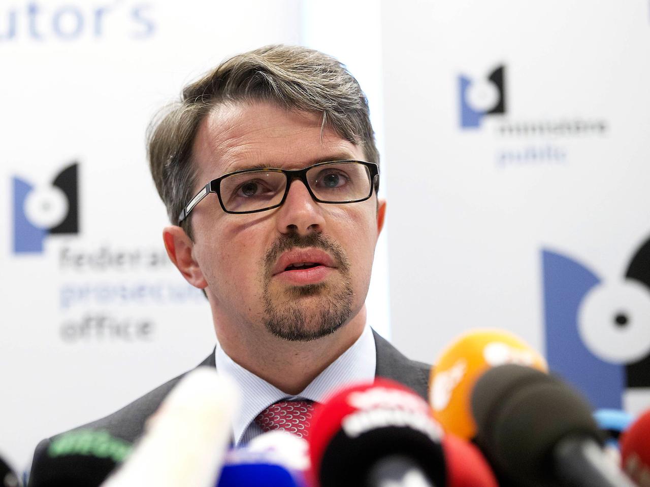 Frederic Van Leeuw hinter mehreren Mikrofonen, im Hintergrund eine Stellwand der Generalstaatsanwaltschaft Frederic Van Leeuw hinter mehreren Mikrofonen, im Hintergrund eine Stellwand der Generalstaatsanwaltschaft