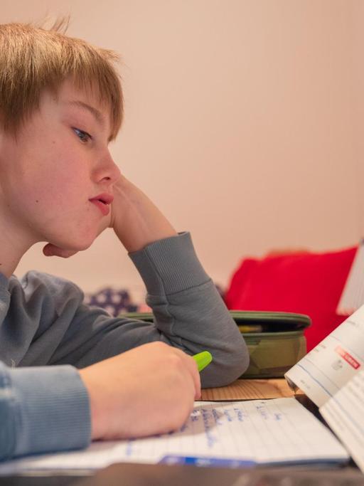 Ein Junge sitzt im Heimunterricht grübelnd über seinen Hausaufgaben.