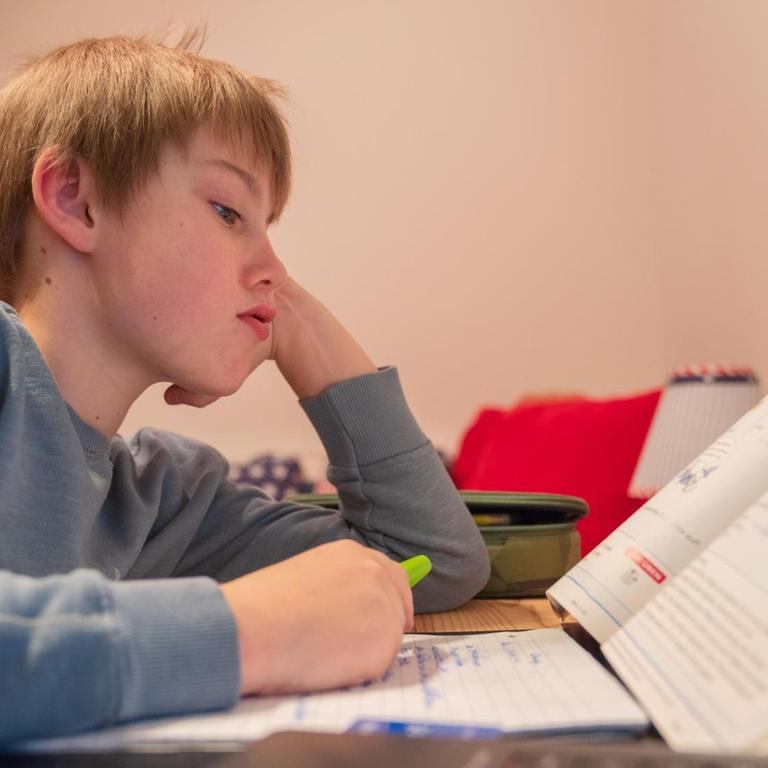 Ein Junge sitzt im Heimunterricht grübelnd über seinen Hausaufgaben.