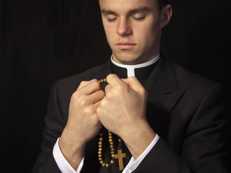 Junger Priester mit geschlossenen Augen, in den Händen einen Rosenkranz.