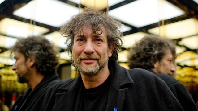 Der Science-Fiction-Autor Neil Gaiman vor einem Spiegel, rechts und links von ihm spiegelt sich sein Hinterkopf.