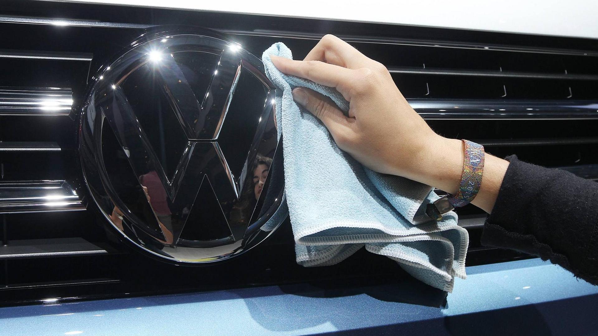 Eine Hand wischt mit einem Tuch über den Rand des VW-Logos an einem Auto. Eine Hand wischt mit einem Tuch über den Rand des VW-Logos an einem Auto.