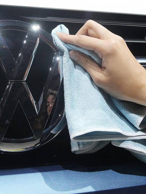 Eine Hand wischt mit einem Tuch über den Rand des VW-Logos an einem Auto.