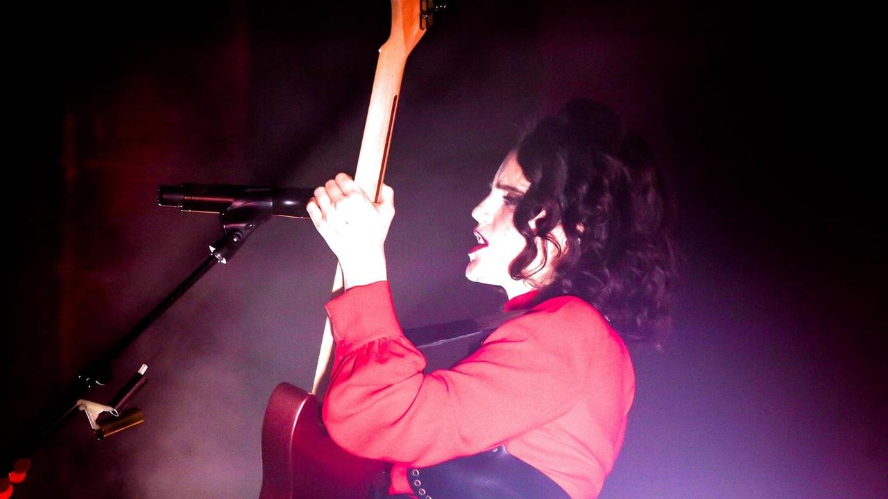 Eine Frau steht auf einer Bühne mit einer Gitarre in der Hand.