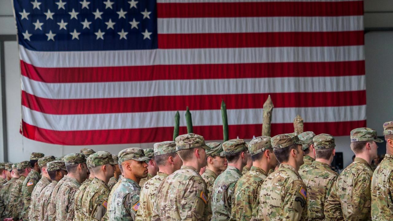 US-Soldaten stehen vor einer amerikanischen Flagge.